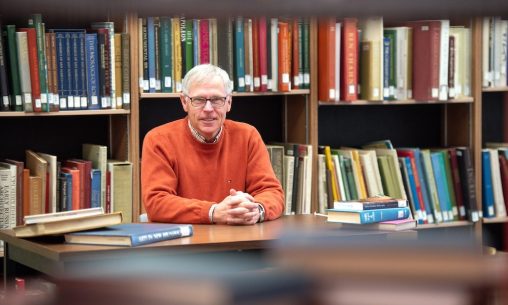 UPEI professor of history Ed MacDonald seated in front of library book stacks